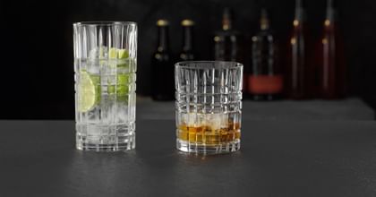 The NACHTMANN Highland Square longdrink glass filled with a clear drink with lime and ice cubes and the tumbler filled with Whiskey on the rocks.