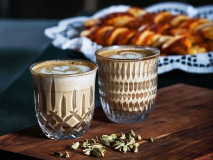 The NACHTMANN Barista Ethno and Noblesse Cappuccino/Flat White glass filled with coffee with pastries in the backdrop