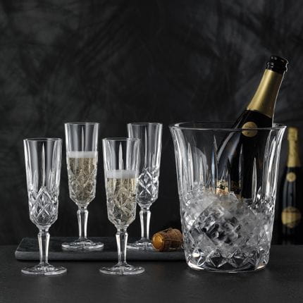 Four NACHTMANN Noblesse Champagne glasses two of which are filled with Champagne. Next to them is the NACHTMANN Noblesse Champagne cooler with ice cubes and an open bottle of Champagne inside.<br/>