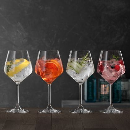 Four SPIEGELAU Gin and Tonic glasses on a wooden table, each of them filled with a different Gin cocktail.<br/>
